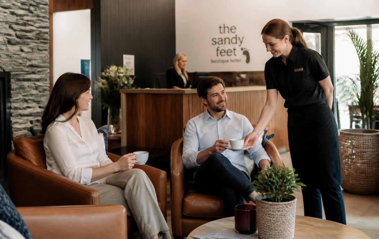 Guests in a boutique hotel lounge being served coffee by a staff member